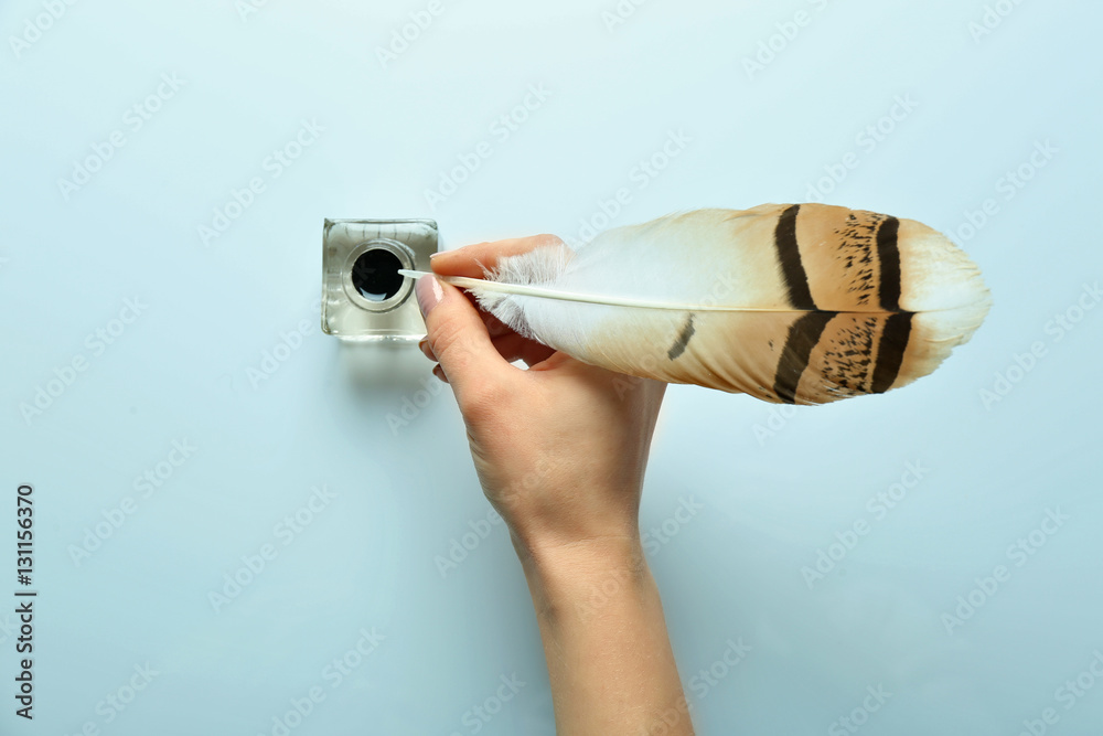 Female hand dipping feather pen into inkwell on light background