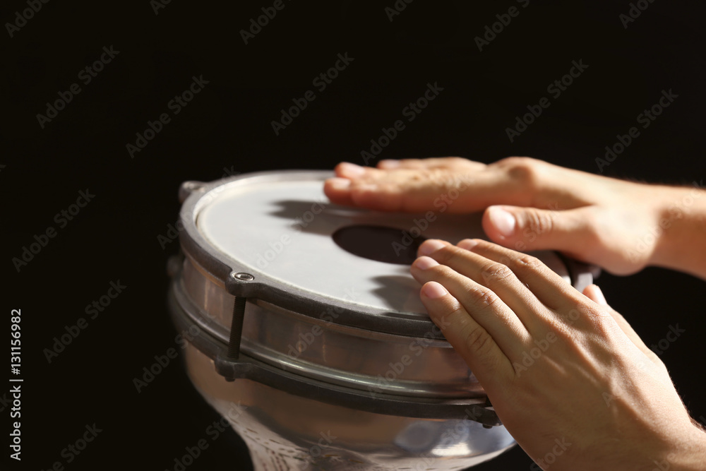 Hands of man playing African drum on dark background