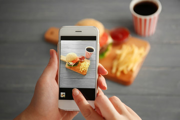 Female hands taking photo of tasty burger with snacks on table