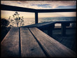 Empty wooden bench on ocean shore at sunset closeup. Vintage retro look and feel