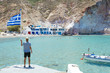 © Westend61 - Greece, Milos, Firopotamos Beach, man looking at sea, holding onto Greek flag