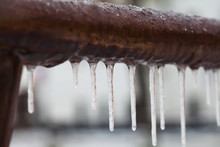 Icicles Hanging From A Brown Pipe. Frozen Water And Metal Surface, Winter Time Concept. Selective Focus Shallow Depth Field