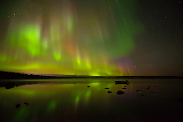 colors of light - colorful northern lights bright up the starry night sky and a calm rocky lake.