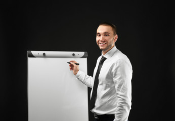 Poster - Young businessman standing near flip chart on black background