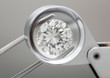 loose brilliant round diamonds is being held by tweezers and looked through a loupe