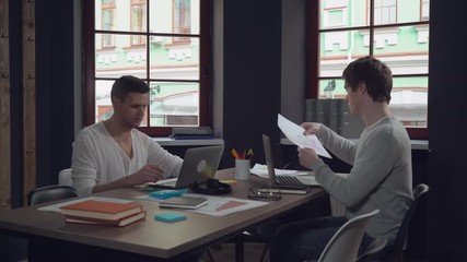 Aufkleber - Young professional start up team working in modern office. Caucasian men computing on laptop and discussing project. Handsome man wearing in casual clothes talking with friend at work. Smiling workers