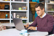 © Dezaypro gmail com - Happy young man smiling, as he works on his laptop to get all his business done early in the morning with his cup of coffee