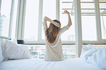 Woman stretching in bed, back view