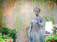 Sculpture Of Woman In A Garden With Brick Background