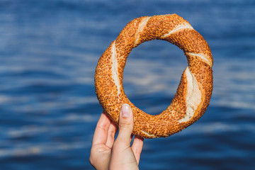 Wall Mural - Woman hand holding a traditional Turkish simit on sea background