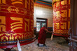 Old bouddhist monk, a tibetan man, spins a huge prayer wheels at the Shechen monastery, Kathmandu, Nepal.
