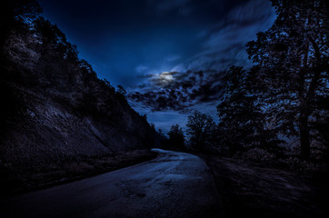 Landscape of night view of roads with bright moon and among stone hill from one side and forest from other