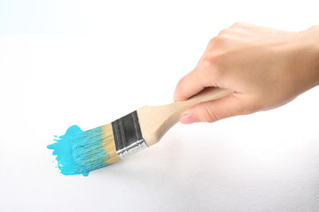 Female hand painting white wall with brush