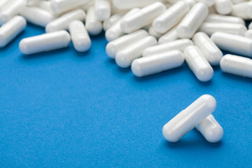 Wall Mural - Medications on blue background. Close up of a pile of white capsules pills. High resolution product. Health care concept