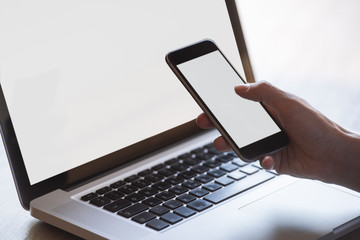 close up multitasking woman using laptop and cellphone, with blank screens, indoors on a table