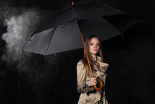 Young Blonde Woman In Classic Trench Coat With Umbrella In Rain Isolated On Black Background