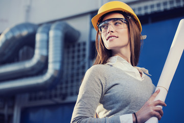 Wall Mural - beautiful woman engineer is standing in front of an industrial pipes background