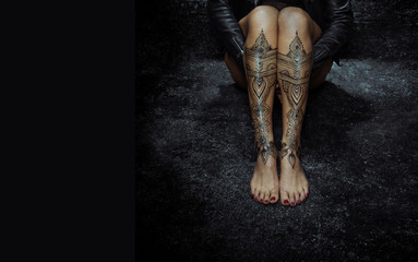 Closeup woman legs with henna tattoo over black stone floor