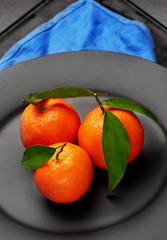 Ripe orange tangerines with green leaves on black ,matt plate . Concept of healthy nutrition, diet, detox. Selective focus.Closeup