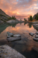 Wall Mural - Rocks And Trees Reflecting In Pink Waters Of Sunset Mountain Lake, Altai Mountains Highland Nature Autumn Landscape Photo