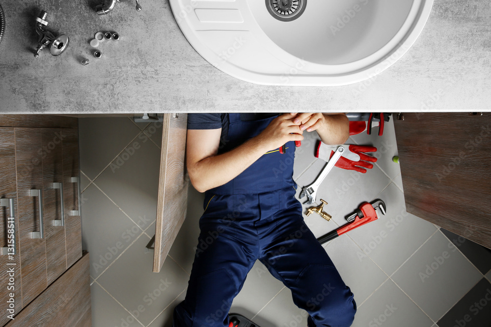 Male plumber repairing sink pipes in kitchen, top view