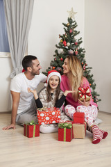 Wall Mural - Young family sitting in front of Christmas tree opening presents