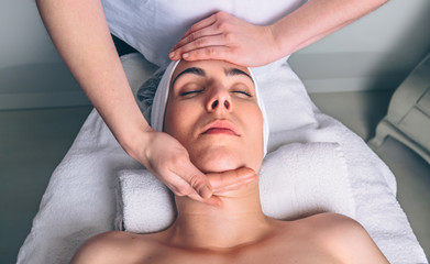 Close up of young woman with closed eyes receiving facial massage on a clinical center. Medicine, healthcare and beauty concept.