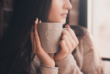 Brunette woman 20-24 year old holding ceramic cup of tea closeup. Looking at window. Good morning. Selective focus. 20s.