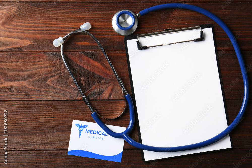 Business card, clipboard and stethoscope on wooden background