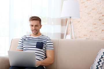 Young man with laptop on sofa in the room