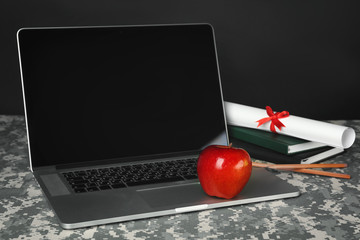 Canvas Print - Military education concept. Open laptop, books and apple on camouflage table closeup