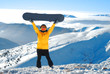 Girl raises snowboard up against panoramic winter mountains