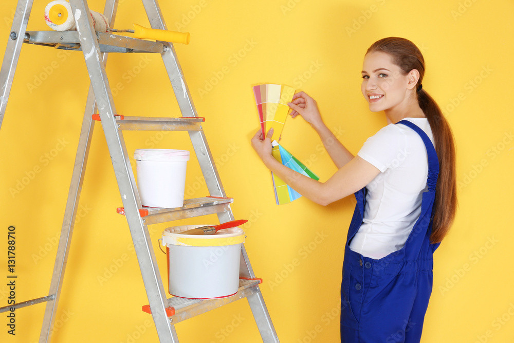 Beautiful young decorator selecting color of wall, on yellow background