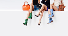 Many Colorful Woman Shoes And Bag Accessories. 3 Women Sitting Together On The White Wall. 