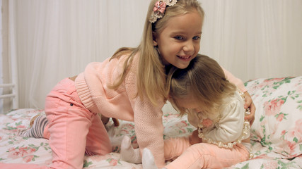 cheerful little girls playing with beads on a bed