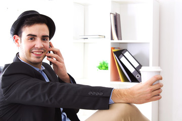 young man talking to the mobile phone and taking a coffee in the office