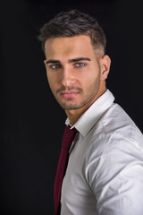 Wall Mural - Handsome young man in in white shirt and red neck tie posing on dark background in studio