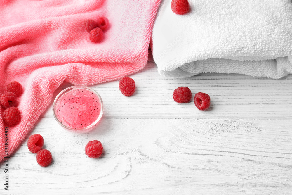 Body scrub in bowl, towels and raspberry on wooden background