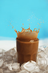 Wall Mural - Glass of cold coffee with ice cubes and splashes on table