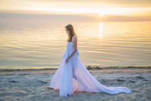Beautiful Girl In A Long White Dress Walking On The Seaside.
