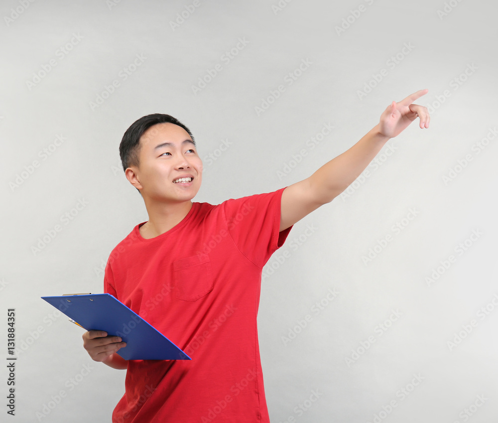 Asian warehouse worker with clipboard pointing at something, on light background