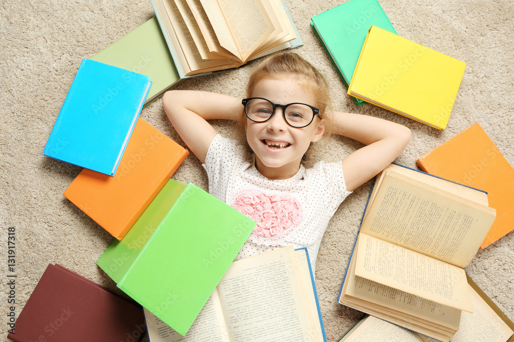 Cute little girl lying on carpet among books