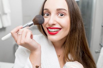 Young smiling woman in bathrobe applying powder in the bathroom