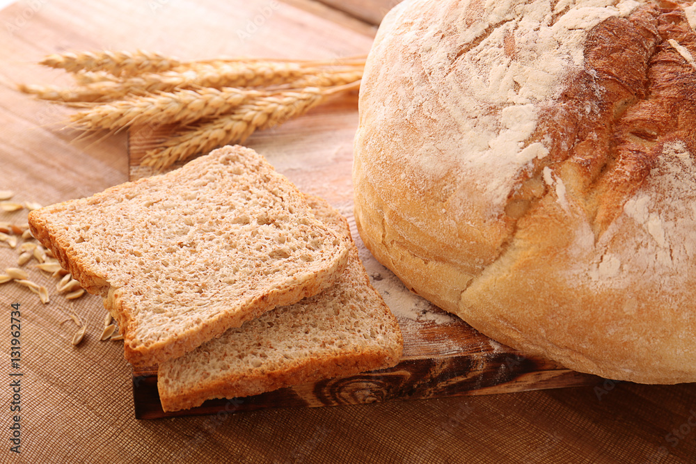 Sliced bread with wheat spikes on wooden table closeup