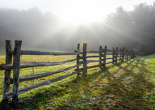 Sun Rays In Foggy Field And Split Rail Fence