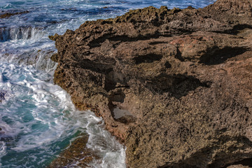 Wall Mural - sea waves crashing against the yellow brown rocks in pacific island. ocean water with white foam.