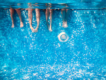 Children's And Adults Legs Underwater In Swimming Pool