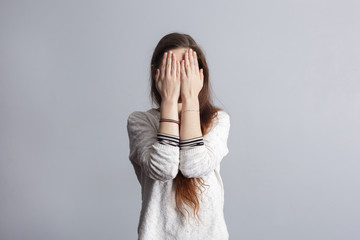 Girl with long hair covers his face with his hands. 