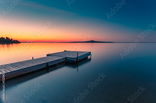 Zdjęcie XXL Drewniane molo na błękitnym jeziorze zachód słońca i gładkie odbicie w wodzie. Długa ekspozycja, jezioro Zerendi, Kazachstan.