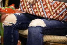 Young Girl Wearing Blue Jeans With The Knees Torn Out Sitting In Chair Holding Gift